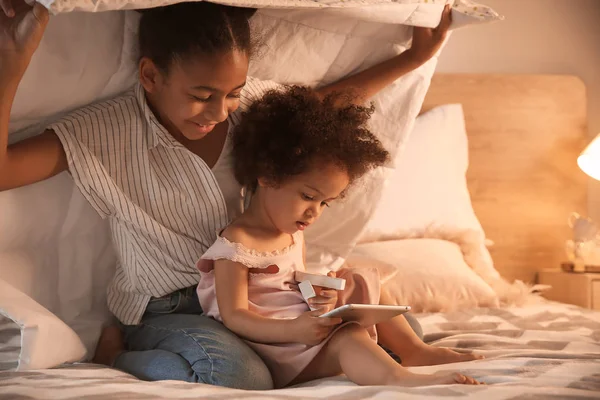 Cute African-American sisters with tablet computer watching cartoons in bedroom — Stock Photo, Image