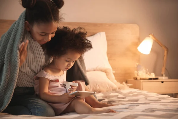 Cute African-American sisters with tablet computer watching cartoons in bedroom — Stock Photo, Image