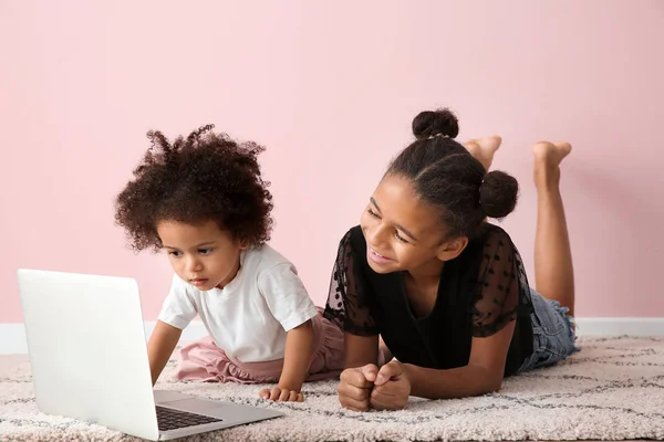 Lindas hermanas afroamericanas con portátil viendo dibujos animados cerca de la pared de color — Foto de Stock