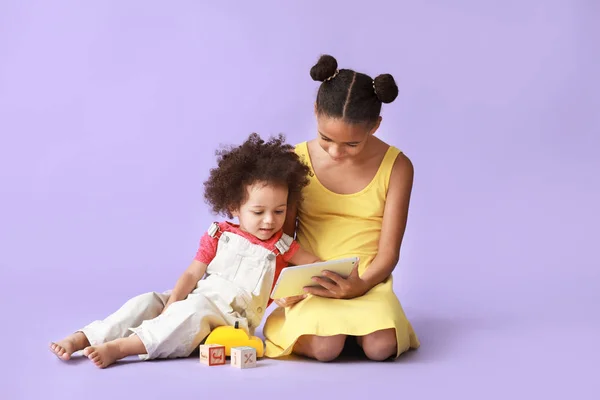 Cute African-American sisters with tablet computer watching cartoons on color background — Stock Photo, Image