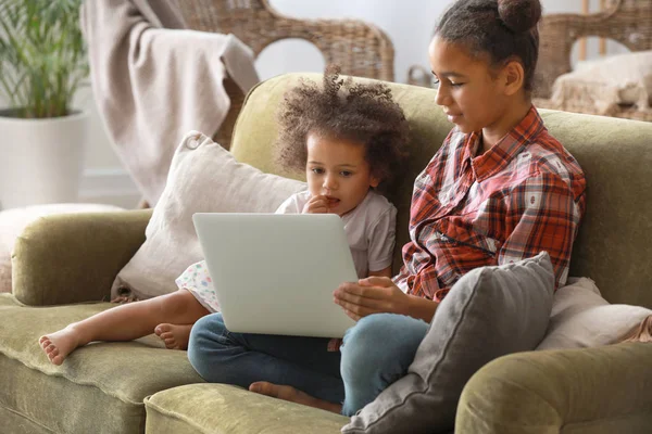 Cute African-American sisters with laptop watching cartoons at home — Stock Photo, Image