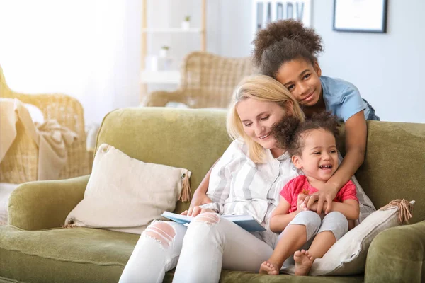 Mujer feliz con sus hijas afroamericanas leyendo libro en casa —  Fotos de Stock