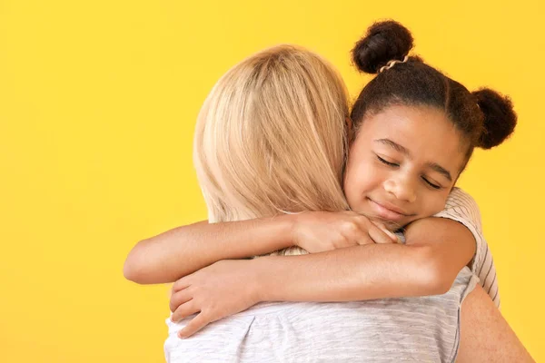 Mujer feliz abrazando a su hija afroamericana sobre fondo de color — Foto de Stock