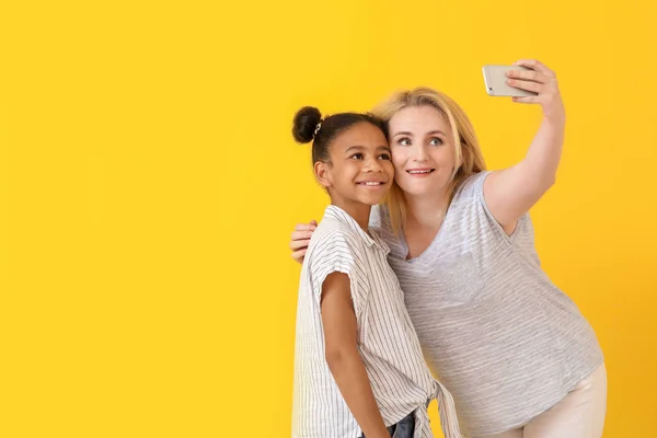 Mulher feliz com sua filha afro-americana tomando selfie no fundo de cor — Fotografia de Stock