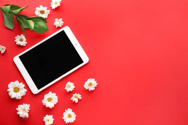 Modern tablet computer with flowers and leaves on color background