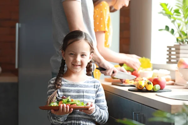 Menina com pais preparando salada de legumes na cozinha — Fotografia de Stock