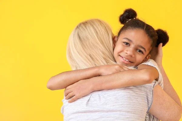 Mujer feliz abrazando a su hija afroamericana sobre fondo de color — Foto de Stock