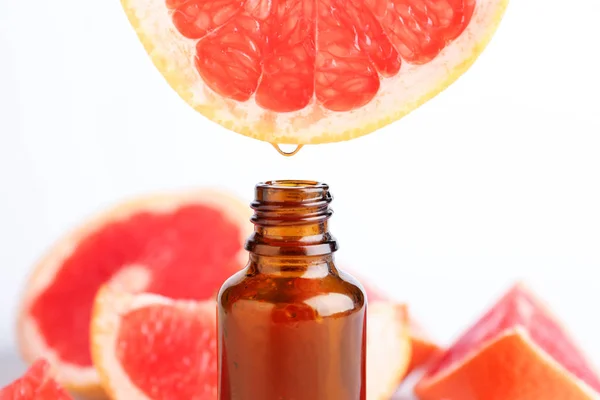 Citrus essential oil dripping from grapefruit into bottle on white background — Stock Photo, Image