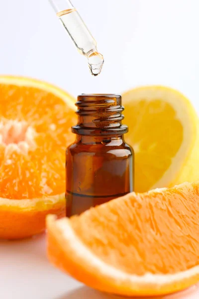 Citrus essential oil dripping from pipette into bottle on white background