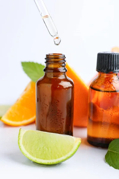 Citrus essential oil dripping from pipette into bottle on white background