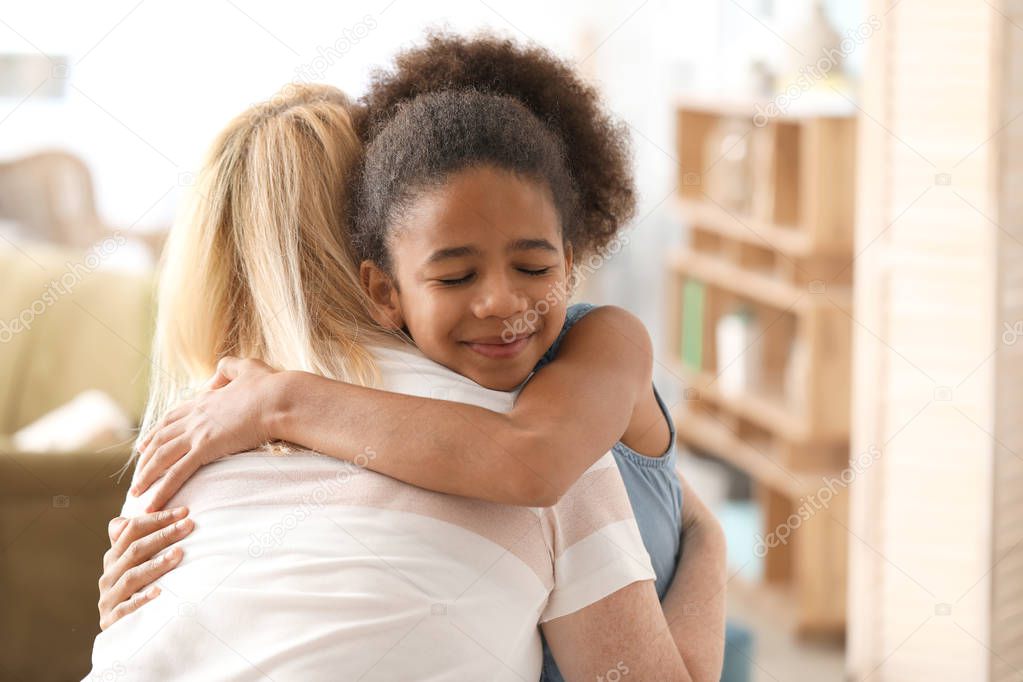 Happy woman hugging with her African-American daughter at home