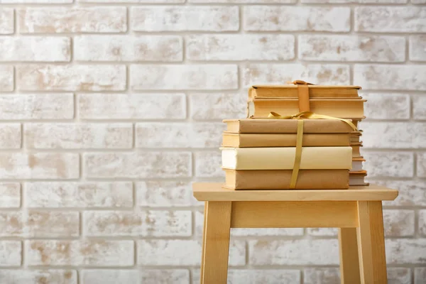 Stacked books on stool against brick wall — Stock Photo, Image