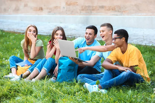 Retrato de jóvenes estudiantes con portátil sentado en la hierba al aire libre —  Fotos de Stock