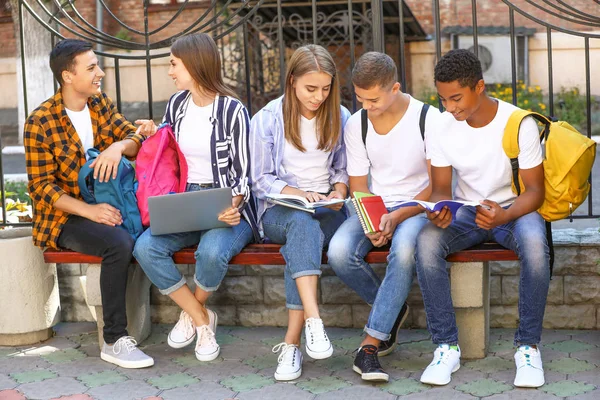 Mladí studenti sedící na lavičce venku — Stock fotografie