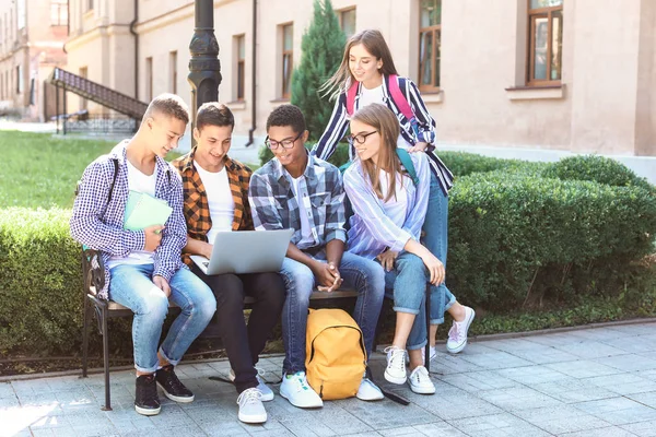 Молоді студенти з ноутбуком сидять на лавці на відкритому повітрі — стокове фото