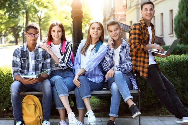 Mladí studenti sedící na lavičce venku — Stock fotografie