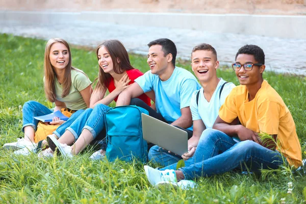 Portrait de jeunes étudiants avec ordinateur portable assis sur l'herbe à l'extérieur — Photo