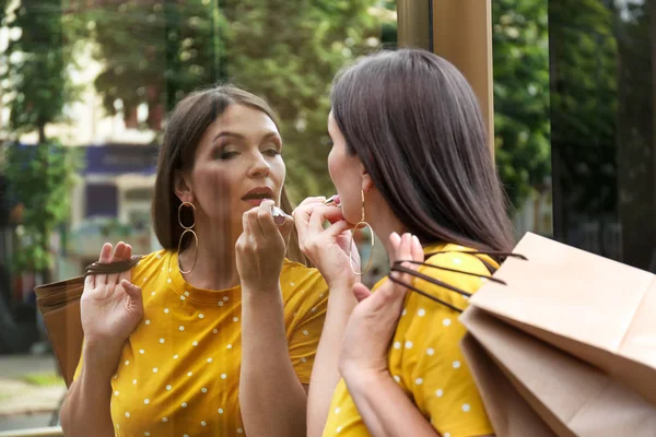 Hermosa mujer que aplica lápiz labial mientras usa escaparate como espejo — Foto de Stock