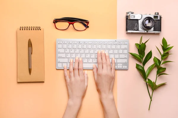 Female hands with PC keyboard, notebook, photo camera and glasses on color background