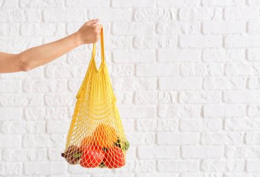 Kadın el beyaz tuğla duvara karşı ürünler ile örgü eko çanta tutarak