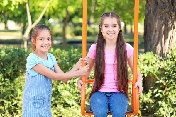 Cute little girls playing on swings in park — Stock Photo, Image