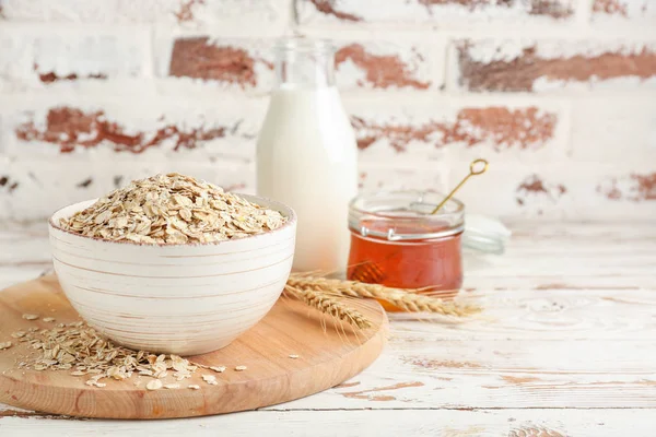 Kom met rauwe havermout, honing en melk op tafel — Stockfoto