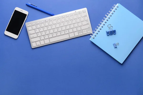 Modern computer keyboard with stationery and mobile phone on color background