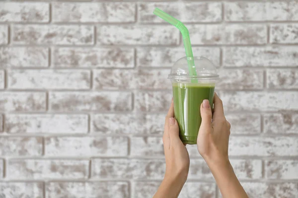 Female hands with tasty green smoothie in cup on brick background — Stock Photo, Image