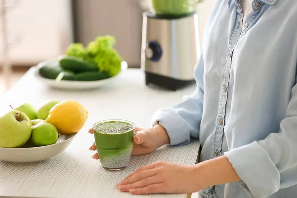 Mulher com vidro de smoothie verde saboroso na cozinha — Fotografia de Stock