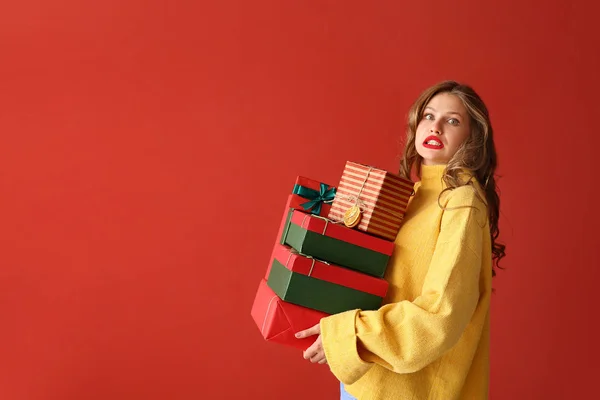 Confused young woman with Christmas gifts on color background — Stock Photo, Image