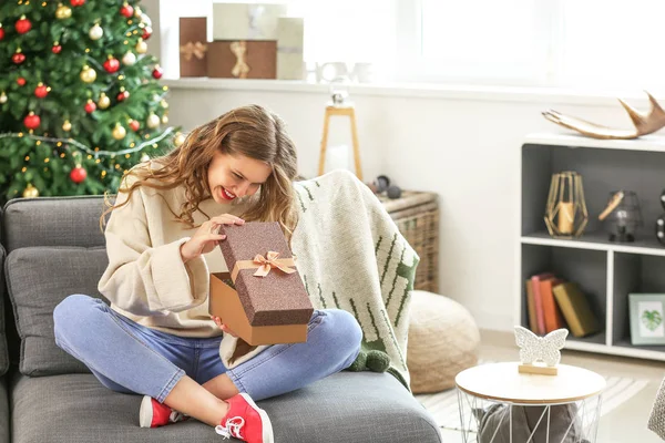 Happy young woman opening Christmas gift at home — Stock Photo, Image