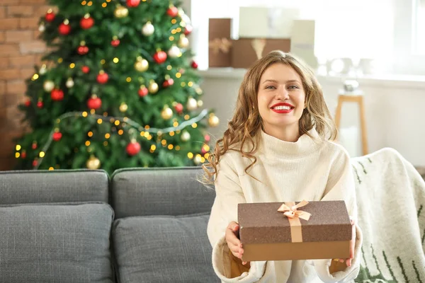 Happy young woman with Christmas gift at home — Stock Photo, Image