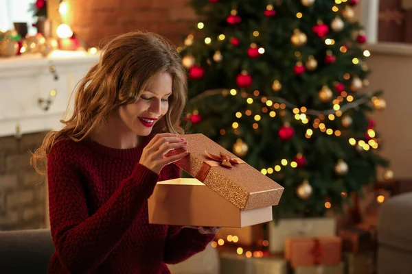 Happy young woman opening Christmas gift at home — Stock Photo, Image