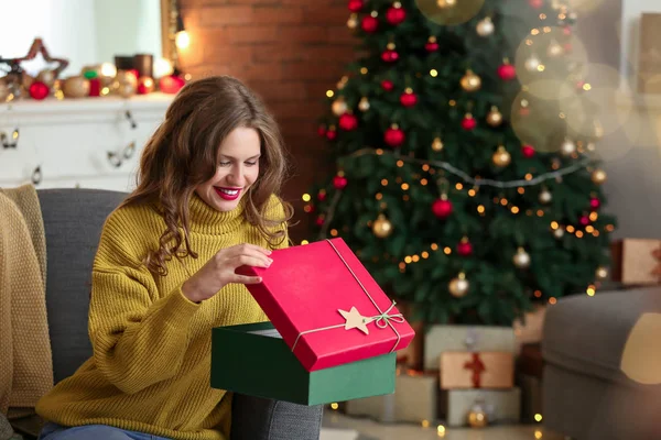 Happy young woman opening Christmas gift at home — Stock Photo, Image