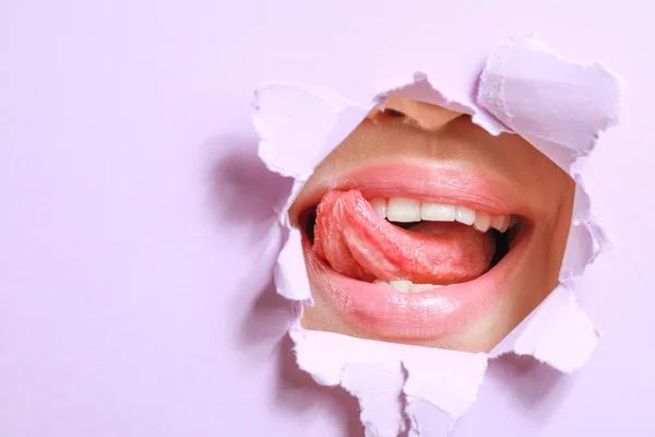 Lippen van mooie jonge vrouw zichtbaar door gat in kleur papier — Stockfoto