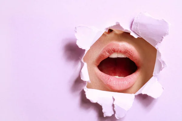 Usta pięknej młodej kobiety widoczne przez otwór w kolorowym papierze — Zdjęcie stockowe