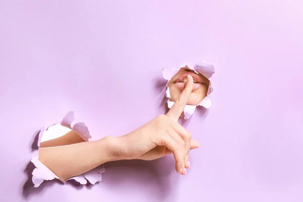 Mujer mostrando gesto de silencio, vista a través de agujeros en papel color rasgado — Foto de Stock