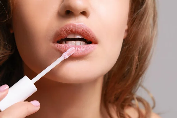 Beautiful young woman applying lipstick against grey background, closeup — Stock Photo, Image