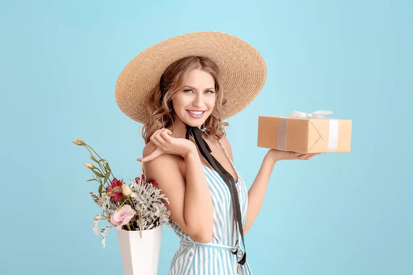 Beautiful young woman with gift box and flowers on light color background — Stock Photo, Image