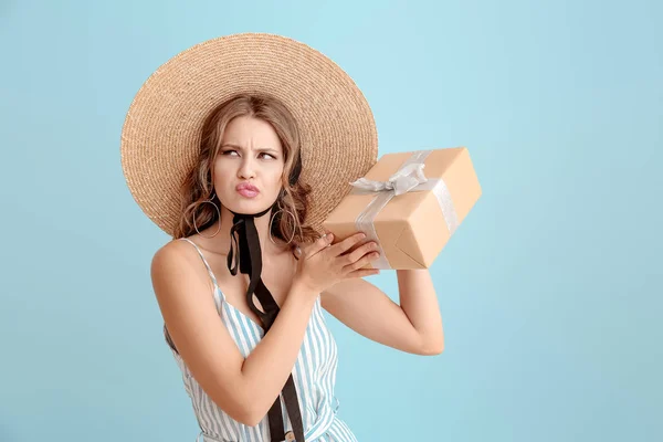 Confused young woman with gift box on light color background