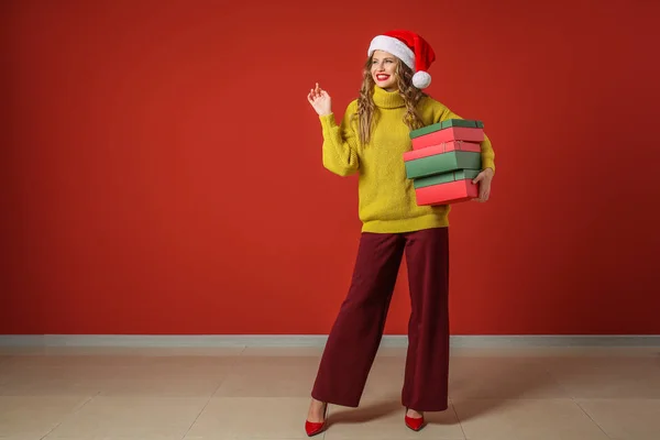 Belle jeune femme avec des cadeaux de Noël près du mur de couleur — Photo