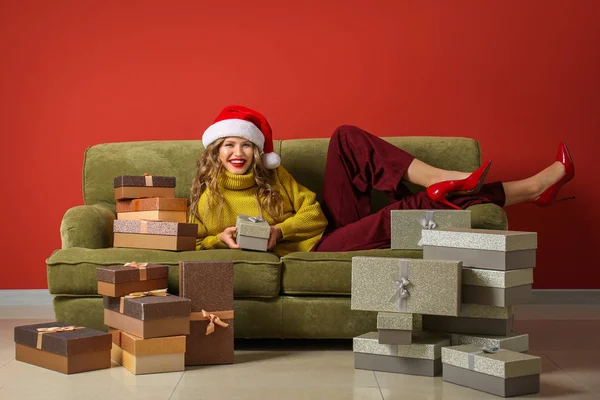 Belle jeune femme avec des cadeaux de Noël couché sur le canapé près du mur de couleur — Photo