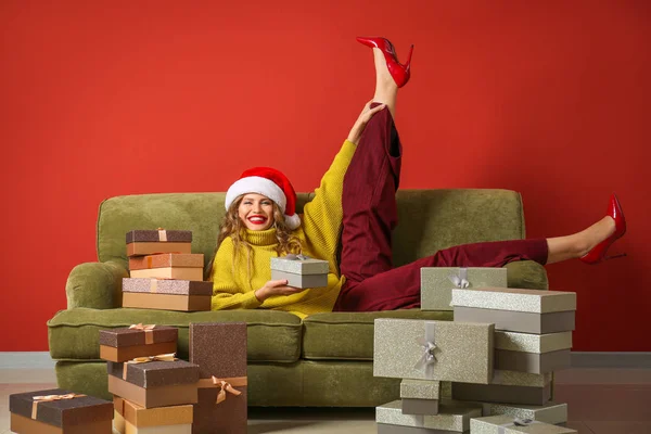 Belle jeune femme avec des cadeaux de Noël couché sur le canapé près du mur de couleur — Photo