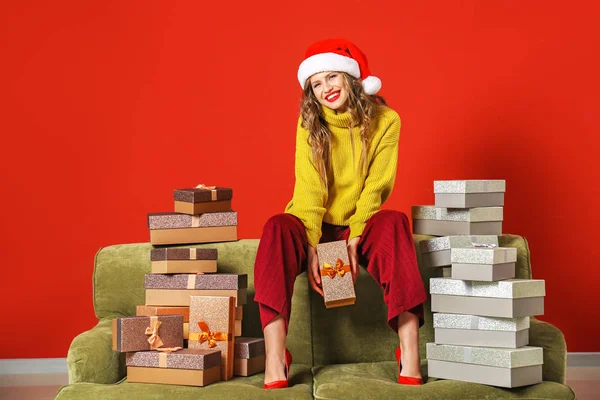 Belle jeune femme avec des cadeaux de Noël assis sur le canapé sur fond de couleur — Photo