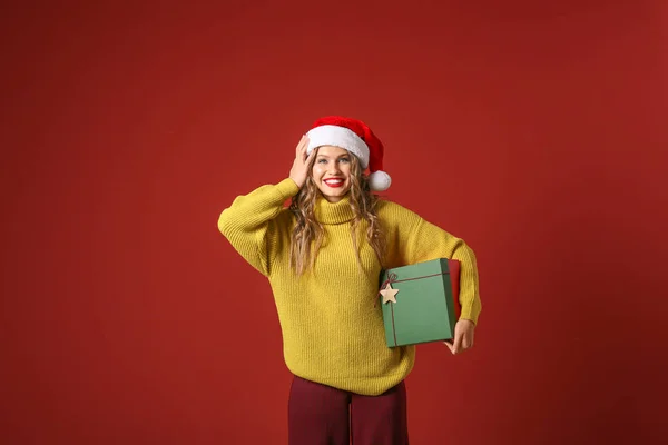 Mooie jonge vrouw met kerstcadeau op kleur achtergrond — Stockfoto