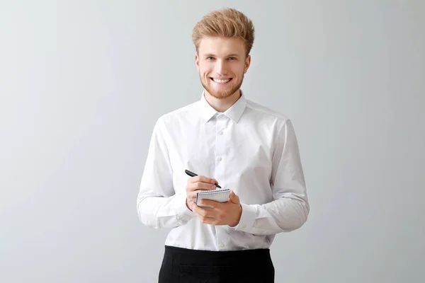 Handsome waiter with notebook on light background — Stock Photo, Image