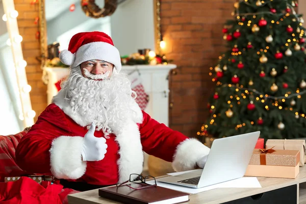 Weihnachtsmann mit Laptop im weihnachtlich dekorierten Zimmer — Stockfoto