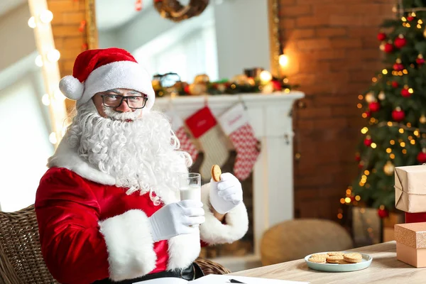 Papai Noel beber leite e comer biscoitos no quarto decorado para o Natal — Fotografia de Stock