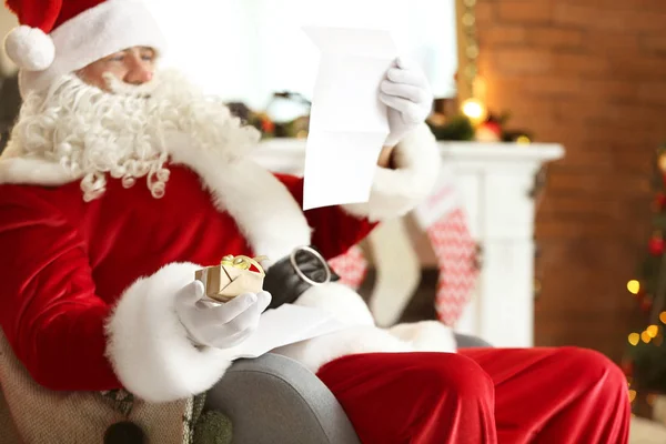 Weihnachtsmann liest Wunschzettel in weihnachtlich dekoriertem Zimmer — Stockfoto