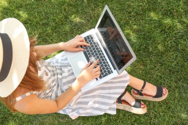 Parkta çim üzerinde oturan dizüstü bilgisayar ile Kadın blogger